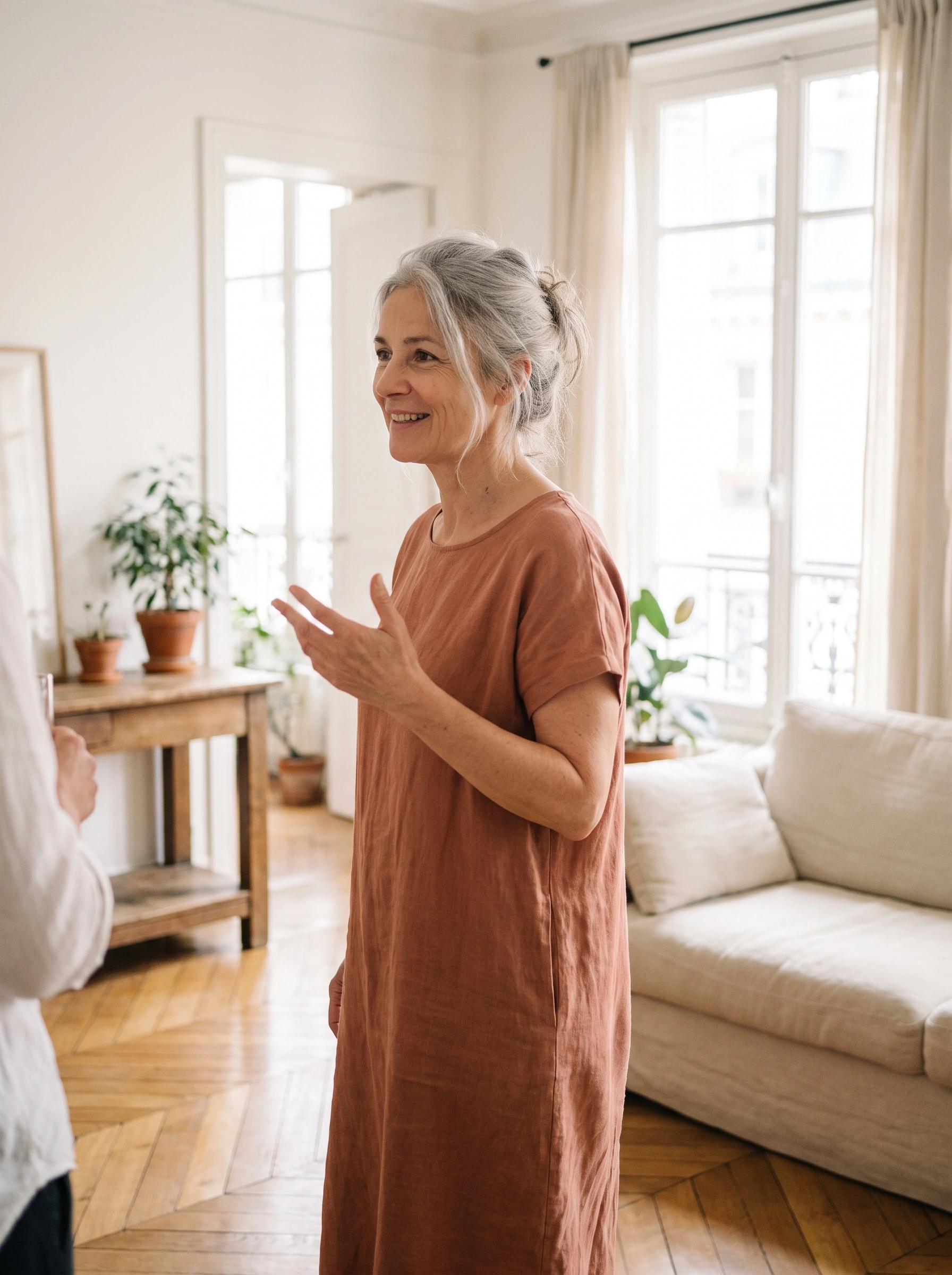 Camille debout dans son salon, en robe, en pleine conversation
